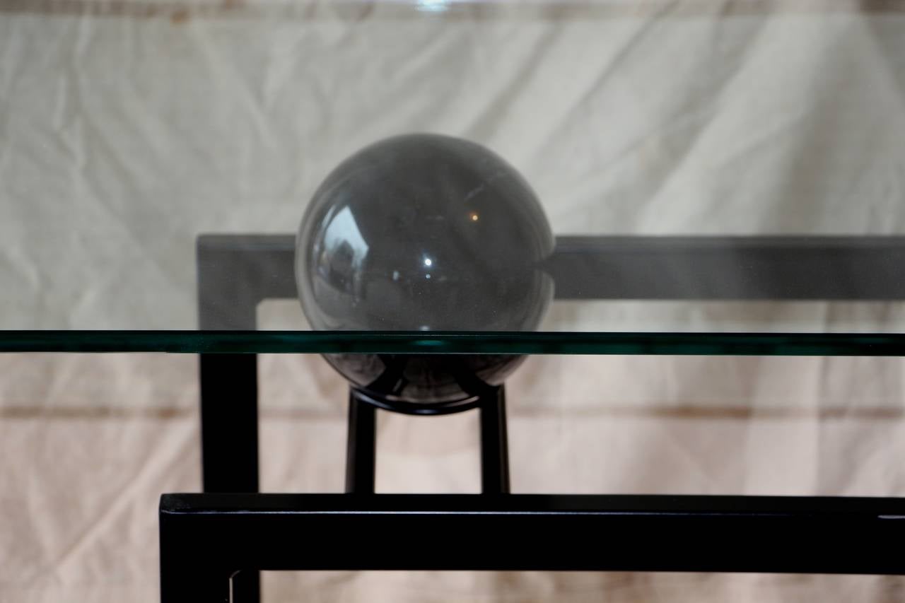 A nicely designed post-modern console with a glass top and a metal base, which features a marble ball support. The black paint has some minor losses.