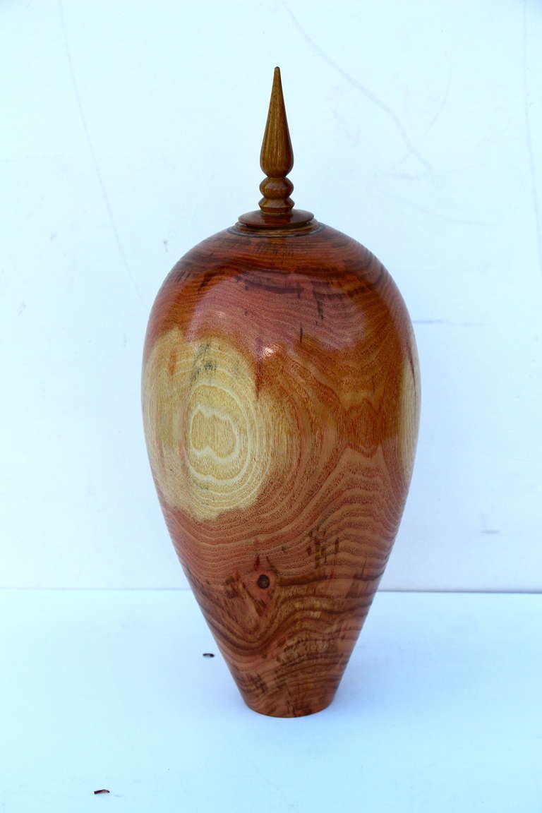 A simply stunning hand-turned vase by the noted Florida wood turner John Mascoll out of honey locust. The top finial is fitted in not glued. The top of the finial has some cracks and has been repaired. Elegant color, graining and design. Signed on