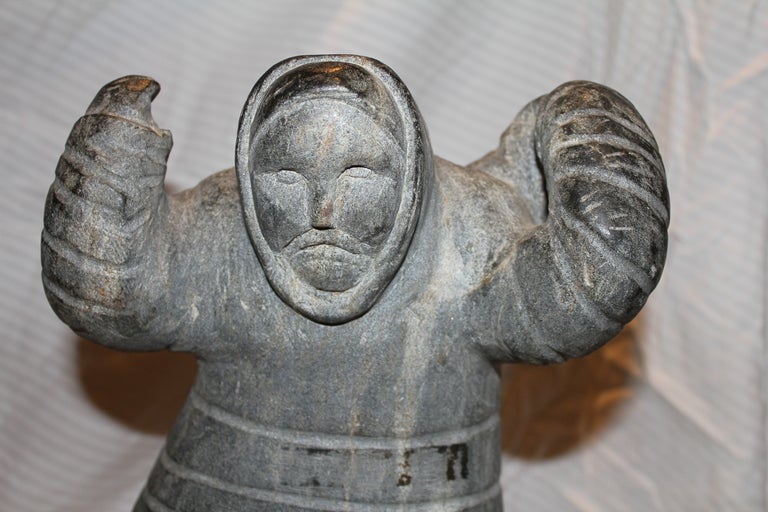 A beautiful hard stone carving of an Eskimo or Inuit hunter carrying a seal. It is missing something perhaps a rope that went from his hand to the remnants of the rope on the seal's back. Mounted on a slate black base. The sculpture is attached with