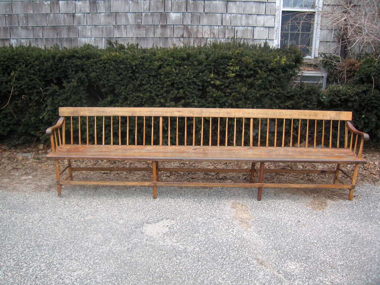 a very long and shakeresque wood bench found in New England with graceful arms and iron brace on each