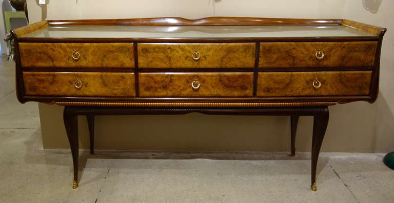 An Italian Mid-Century sideboard/credenza in the style of Osvaldo Borsani of rectangular form with gently flared sides of equal height to that of the shaped back rail surrounding the glass top over six drawers with brass pulls finished with a beaded