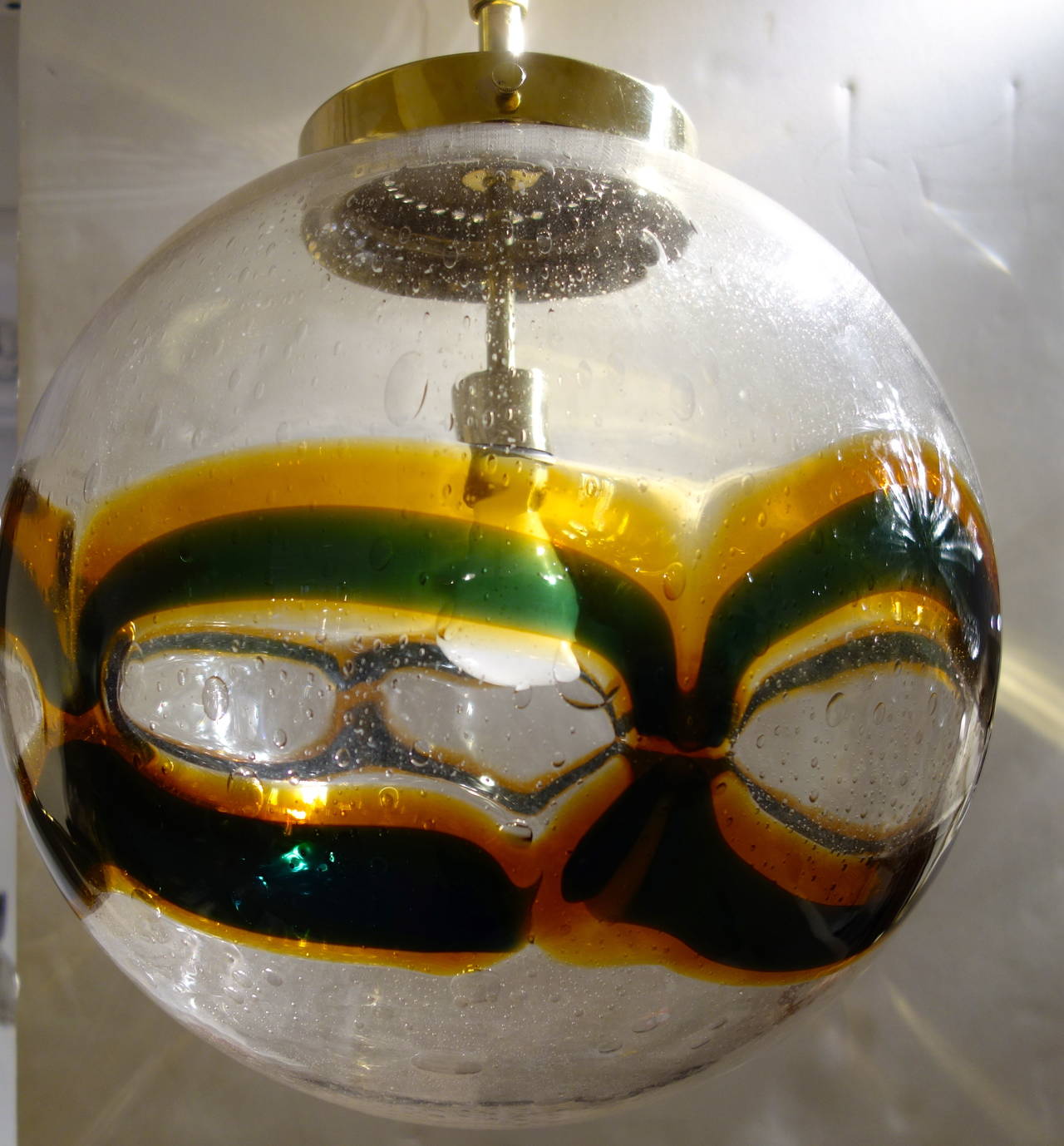 A midcentury handblown Murano globe of clear heavy glass with all-over internal bubbles with an undulating double helix of amber and dark green, the fixture suspended by a custom brass shaft and canopy newly wired for the American market