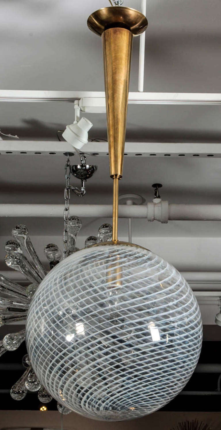 An Italian Mid-Century handblown Reticello Murano glass globe/chandelier/pendant featuring white spiral design on clear glass suspended by an Italian contemporary custom brass pole and canopy designed to cover American light boxes, newly wired with