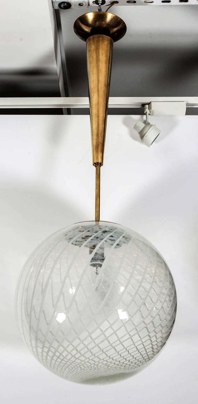 An Italian Mid-Century handblown Reticello Murano glass globe/chandelier/pendant featuring a white spiral design on clear glass suspended by an Italian contemporary custom brass ploe and canopy designed to cover American light boxes, newly wired