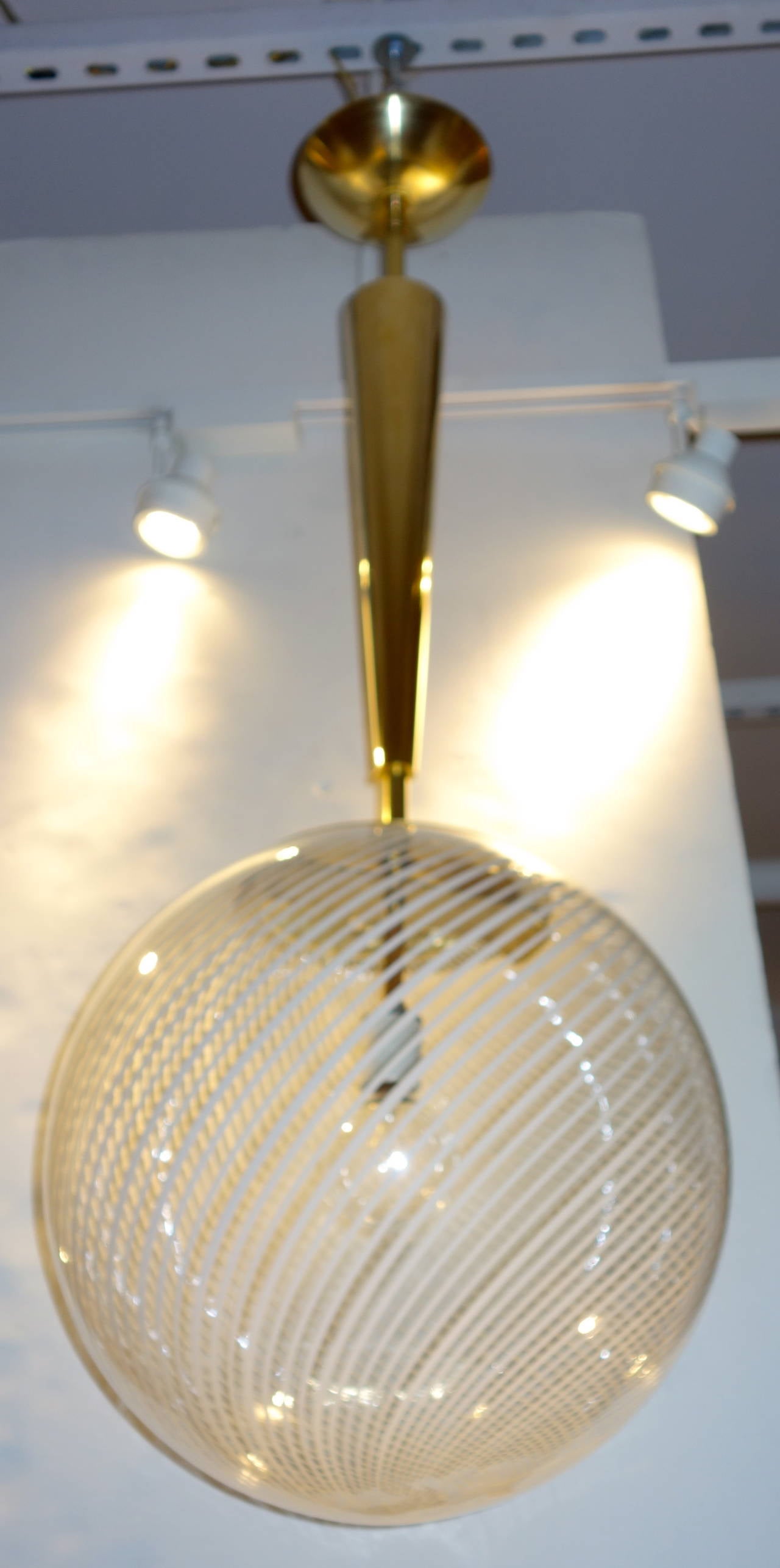 An Italian Mid-Century hand blown Reticello Murano glass globe/chandelier pendant featuring a white spiral design on clear glass suspended by an Italian contemporary custom tapered brass cone and canopy newly wired with a single socket that can