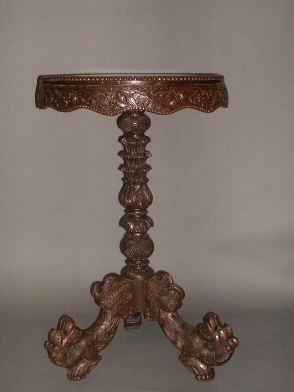 An early 19th century Indo-Portuguese circular rosewood tilt-top side table, the top featuring a three inch jungle scene border with a scalloped apron of foliate design resting on an intricately carved column terminating in a tripod base of serpent