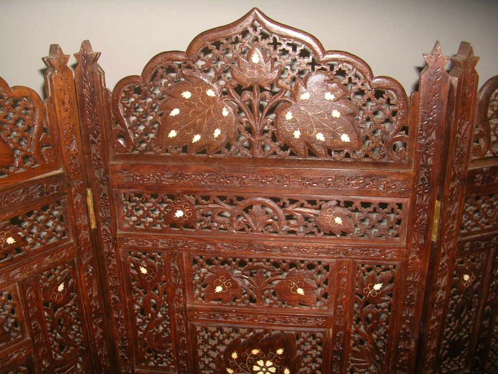 An unusual early 20th century folding hand carved rosewood screen, one side with leaves inlaid with bone and brass stems, the reverse side inlaid with brass set within pierced latticework of alternating stars and quatrefoils. The true color which is