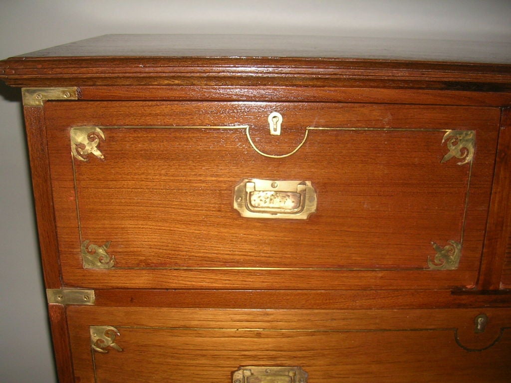 An Anglo-Indian Teakwood two part campaign chest with brass side carrying handles, with two short drawers over three long ones, each inlaid with brass stringing and corner decorations, brass pulls and escutcheons, resting on double bun feet.<br