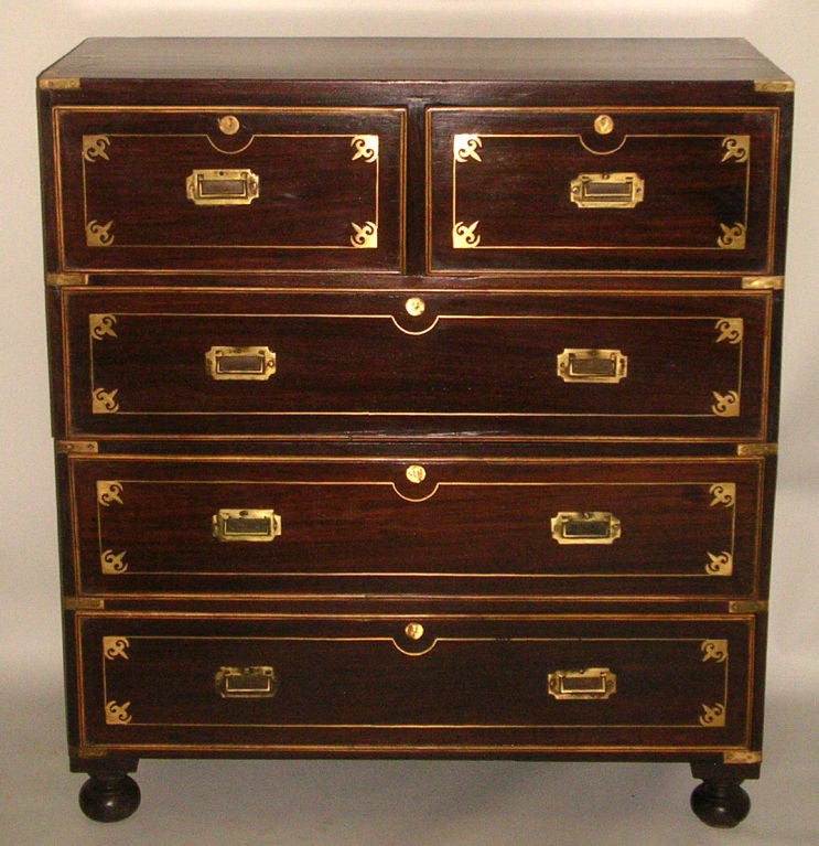 An early 19th century Anglo-Indian rosewood two-part, brass bound campaign chest featuring two short over three long drawers, each trimmed with satinwood and inlaid with brass stringing with four decorative brass corners and escutcheons with