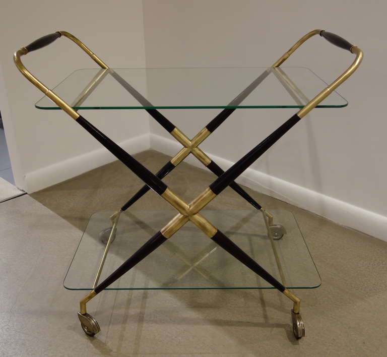 A Mid-Century Italian two tier x- shaped wood and brass bar cart with two glass shelves on roller feet.