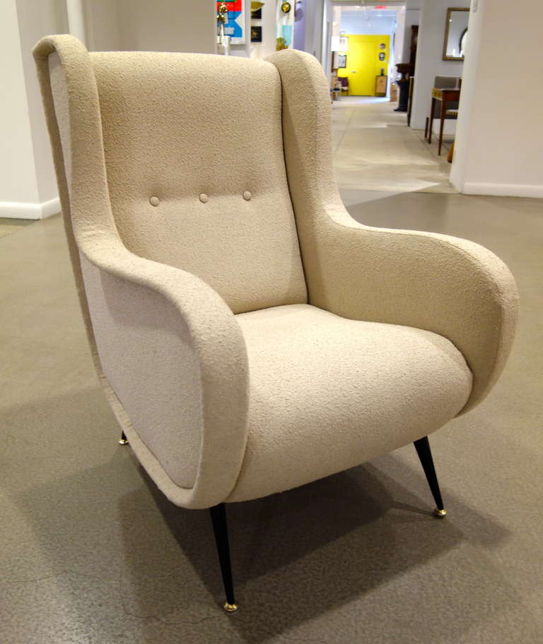 A pair of Mid-Century Italian lounge or armchairs with sculptural flat armrests, tight three button backs and seats resting on painted splayed black metal  brass capped feet newly upholstered in pale taupe boucle fabric.