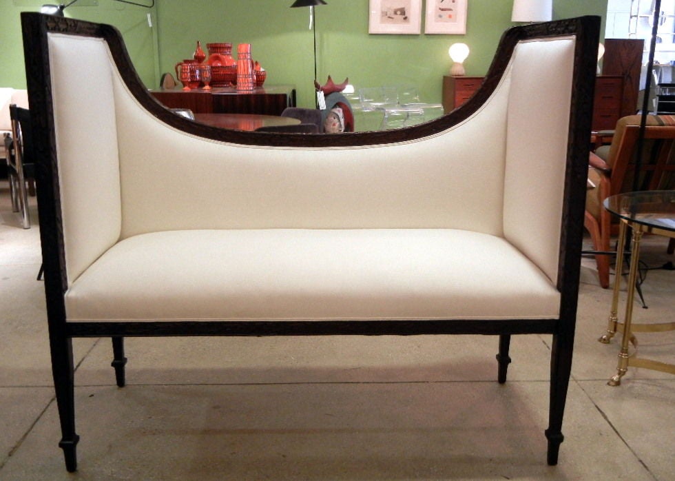 A French turn-of-the century window seat/bench, the dark brown mahogany frame with carved stylized acanthus leaves on the front and sides, the back rest rising on each end, the two tall sides continuing in a straight line forming the legs, newly