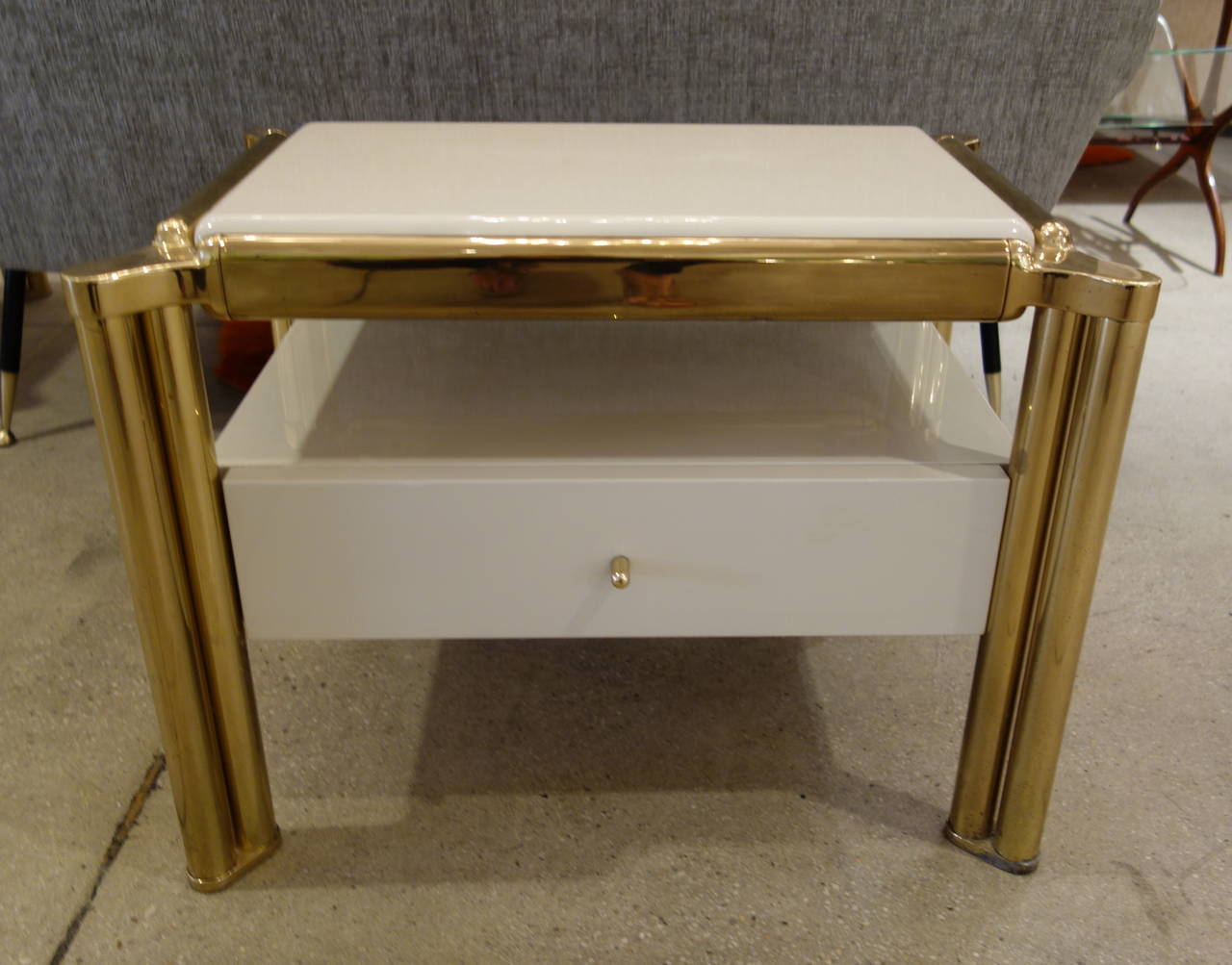 A pair of Italian Mid-Century cream colored lacquered night stands within a substantial tubular brass frame finished on all four sides featuring a floating top over a recessed space with a single brass knobbed pull-out drawer. A companion