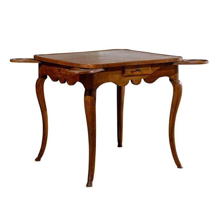 A French period Louis XV walnut game table from the second half of the 18th century, with pull-outs, four drawers, scalloped apron and cabriole legs. This French walnut game table features a square top with rounded corners, sitting above a