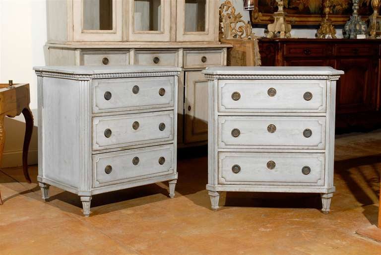 A pair of Swedish Gustavian period three-drawer painted commodes with dentil molding from the early 19th century. Each of this pair of Swedish chests features a rectangular top with protruding canted corners in the front, sitting above a cornice