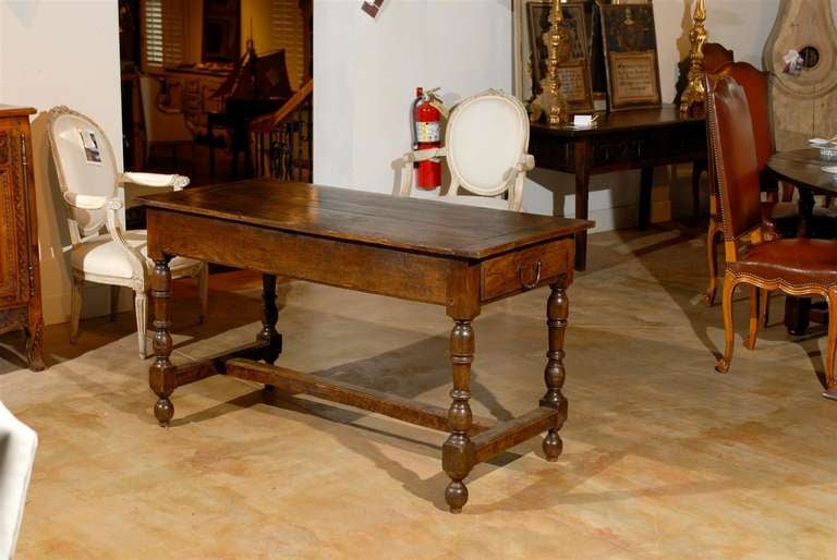 A French Louis XIII style oak sofa table with lateral drawer, turned legs and side stretcher from the mid-18th century. This French oak table features a rectangular planked top sitting above a simple apron, comprising a single lateral hand-cut