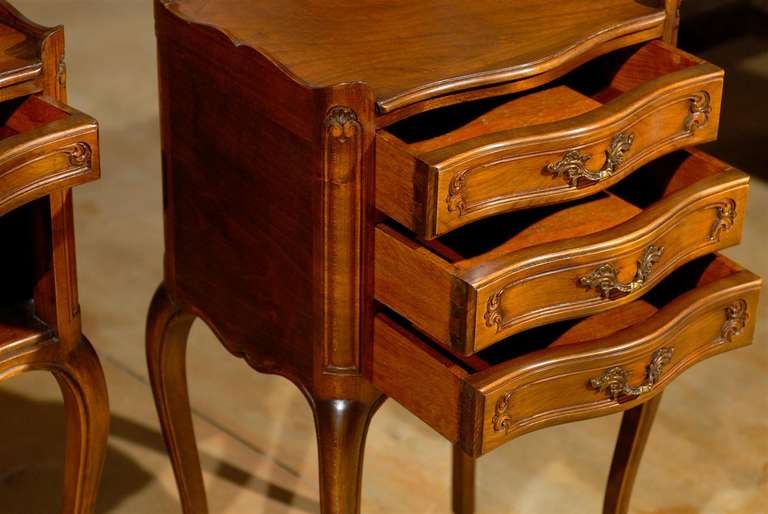 A pair of French Louis XV style walnut bedside tables from the early 20th century. This pair of French 'tables de chevet' was created in the early years of the 20th century, at a time when the country revisited the Rococo style that marked the reign