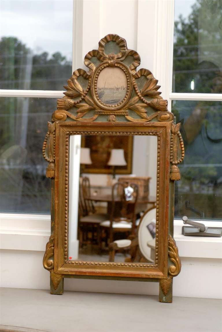 A French Louis XV period painted and gilded mirror from the mid 18th century, with carved crest, petite tassels and grisaille harbor scene. Created in France during the reign of King Louis XV nicknamed Le Bien-Aimé (the Beloved), this wall mirror
