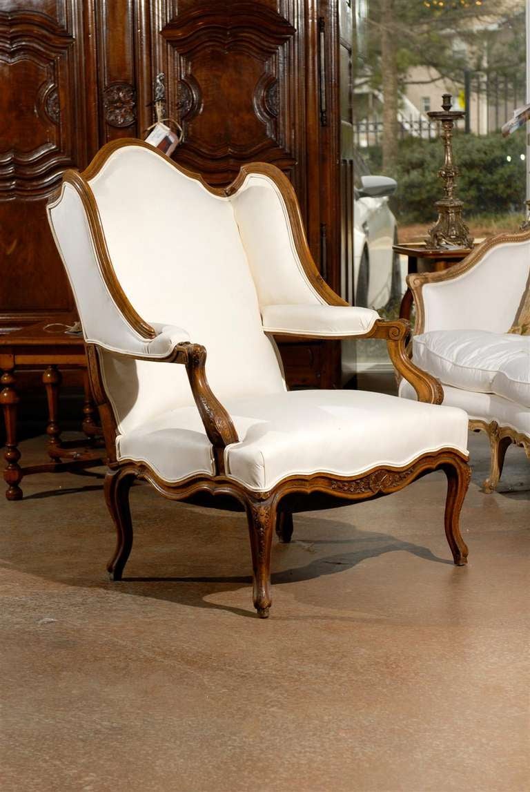 A pair of French Louis XV period walnut confessional bergères armchairs from the mid-18th century with upholstery. Each of this pair of French 'Bergères à oreilles' features a slightly slanted wingback, offering the perfect privacy needed for a