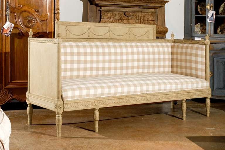 A Swedish period Gustavian Neoclassical upholstered painted wood sofa with beaded swag motifs from the early 19th century. This Swedish painted wooden bench features an exquisite silhouette, typical of the Neoclassical taste for clean lines and