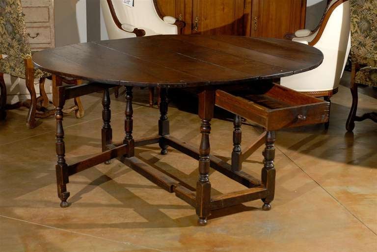 An English Charles II style walnut gateleg drop-leaf table from the late 19th century. This English table features an oval drop-leaf top, sitting above an exquisite turned base. Four central legs support the top as well as a single drawer. Each leg