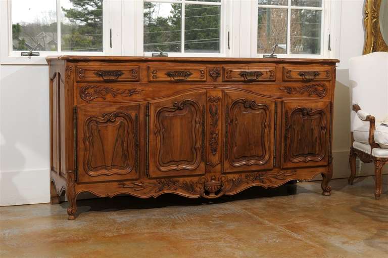 A French Louis XV style walnut four-drawer over four door enfilade with scalloped and pierced apron from the 1950s. This French long walnut buffet features a shaped and raised parquetry top over four drawers. The hardware mounted on each drawer is