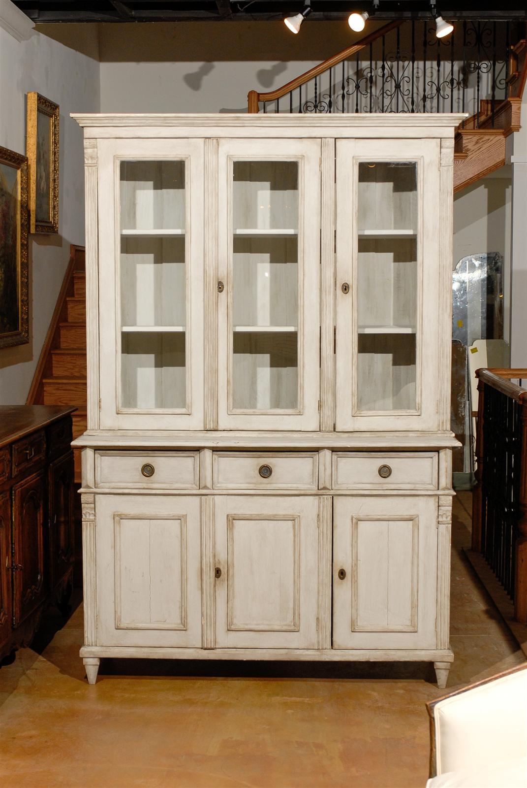 A Swedish Neoclassical style painted wood cupboard with glass doors in its upper cabinet and drawers over doors in the lower one, from the late 20th century. This Swedish cupboard was born in the later years of the 20th century and created in the