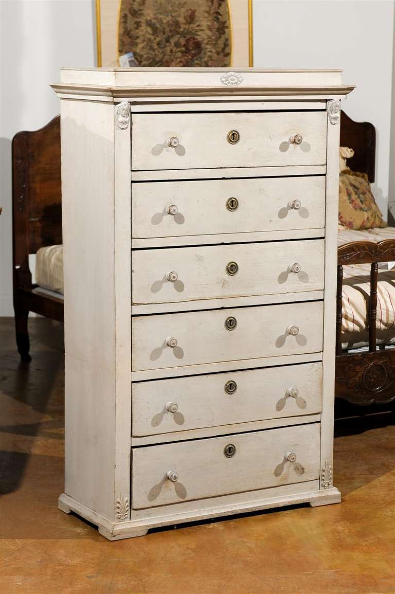 A Swedish neoclassical style mid-19th century wooden tall chest-of-drawers painted in a cream color. This Swedish tall chest features a rectangular raised top adorned in its centre with an oval carved medallion, sitting above a bevelled cornice and