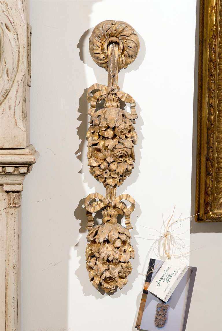 A pair of French Louis XV period carved giltwood appliques from the mid-18th century. Each of this pair of French carved elements features a garland of delicate flowers tied with bows and hanging from an upper medallion adorned with foliage motifs.