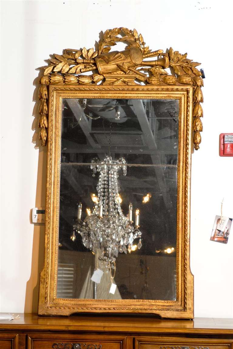A French Louis XVI period giltwood mirror from the late 18th century with original glass and richly carved crest depicting the Liberal Arts. This French giltwood mirror was born in the later years of the reign of King Louis XVI, at a time when