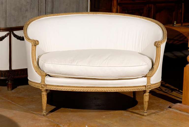 A French Louis XVI style intricately carved sofa with wraparound back and fluted legs from the late 19th century. This French canapé features an exquisite wraparound back adorned with a carved molding on the upper rail. The back flows flawlessly