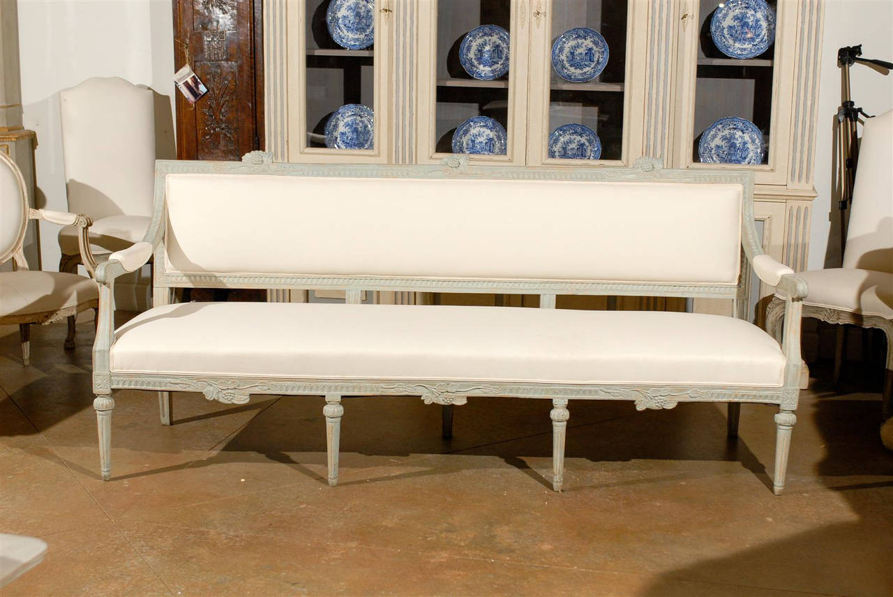 A Neoclassical Revival Swedish carved and painted bench from the late 19th century with scrolled open arms, fluted legs, floral motifs and new upholstery. This Swedish bench features an upright rectangular back that has been reupholstered in a