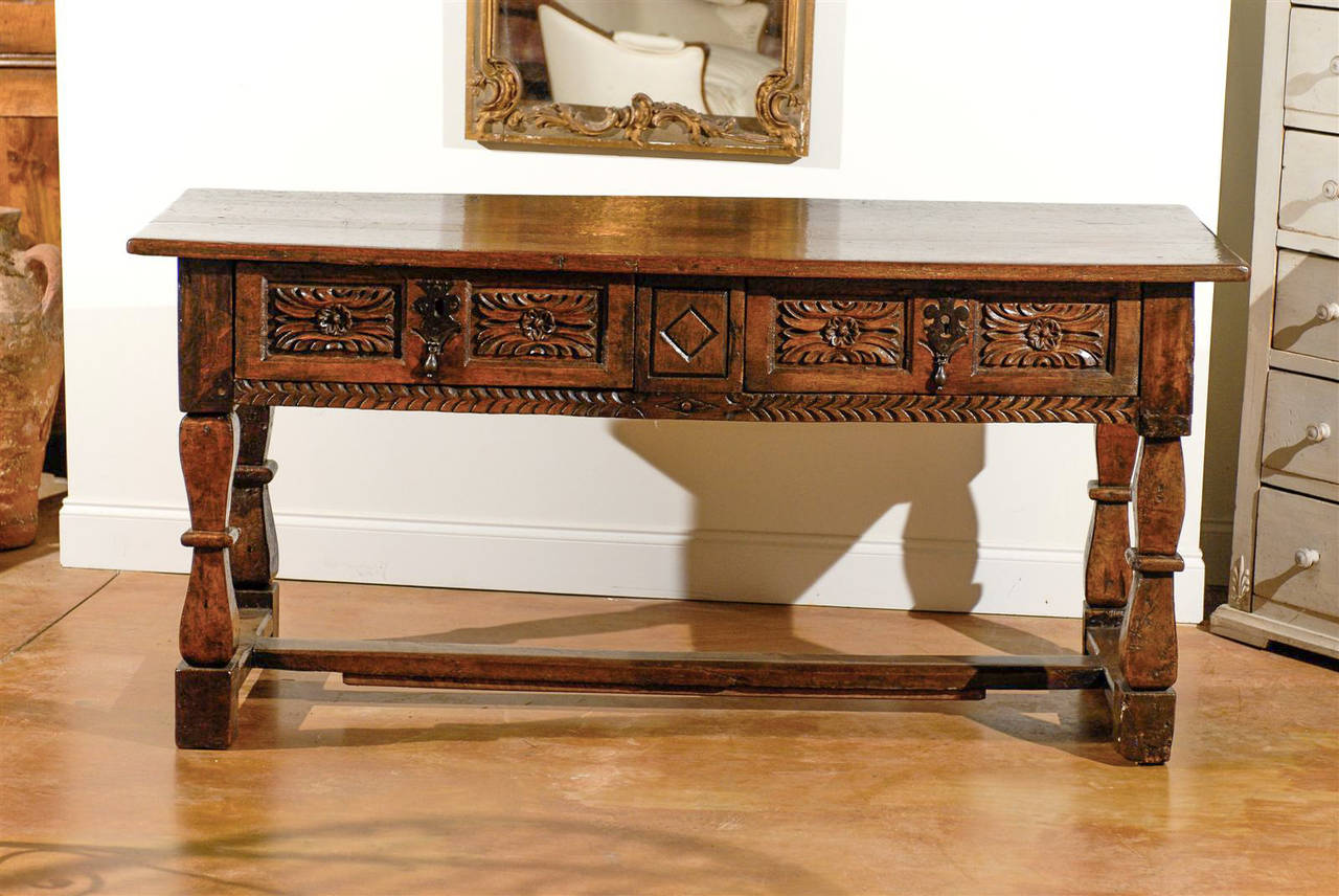 17th century Spanish table with two drawers and hand-forged iron embellishments. Richly carved and detailed on all sides.