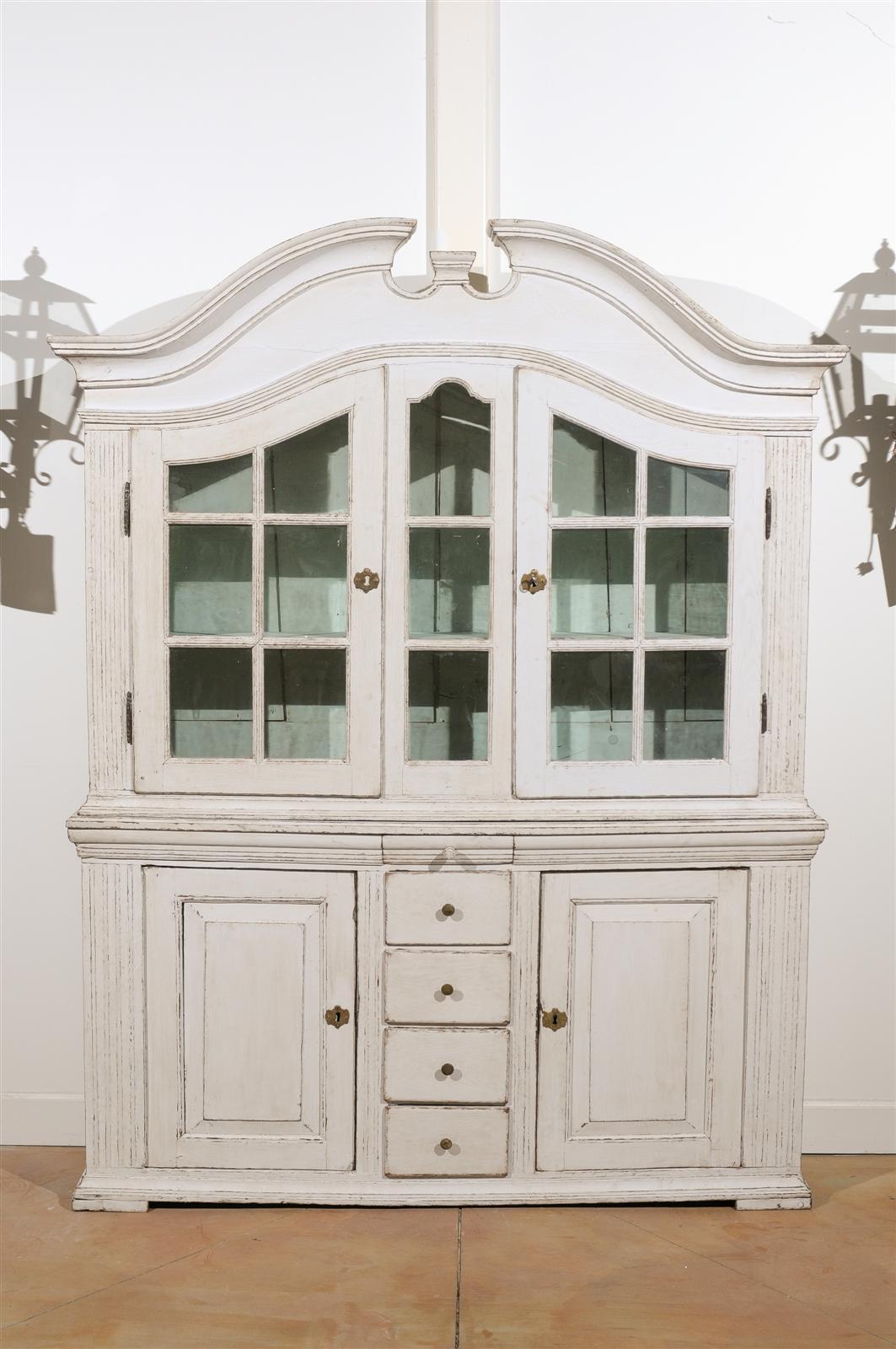 A Swedish painted wood glass door tall cabinet with broken pediment and fluted pilasters from the second half of the 18th century. This Swedish vitrine features an upper cabinet adorned with an eye catching broken pediment, sitting above two shaped