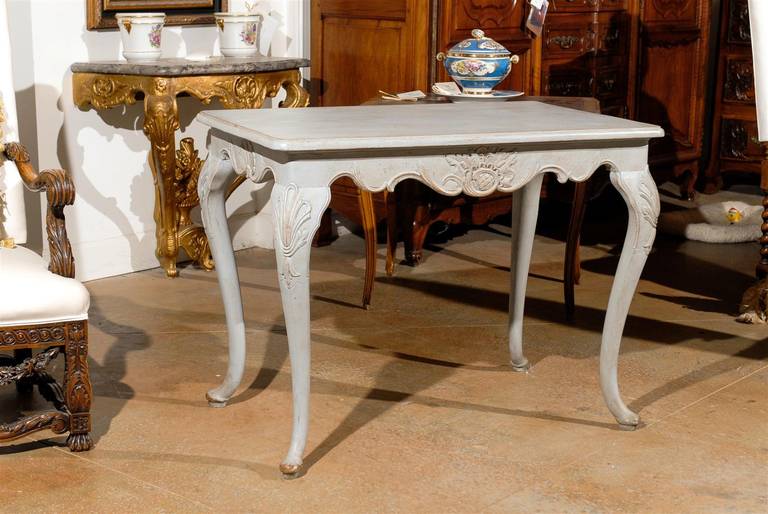 A Swedish Rococo Revival painted wooden side table with carved apron and cabriole legs from the turn of the century. This Swedish side table features a rectangular top with rounded edges sitting above a scalloped apron on all sides, carved with