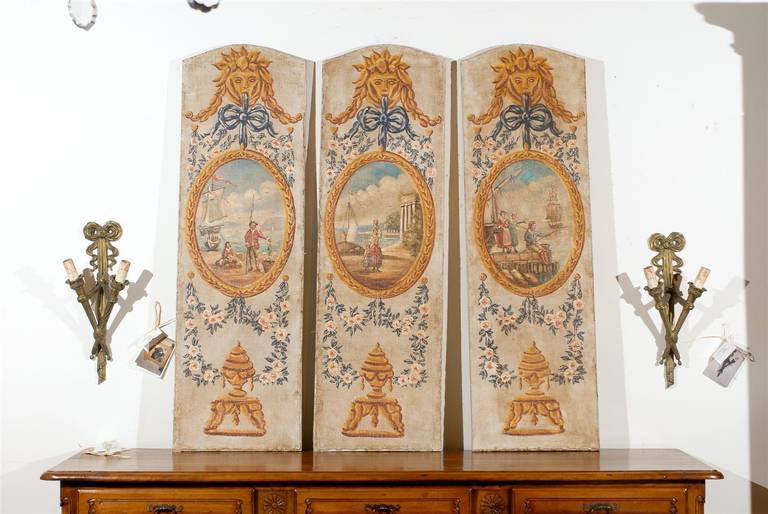 A set of three French Louis XVI style oil on canvas decorative panels from the late 19th century depicting scenes of a French fishing village. Each of this set of French decorative panels features an exquisite painted décor, organized vertically