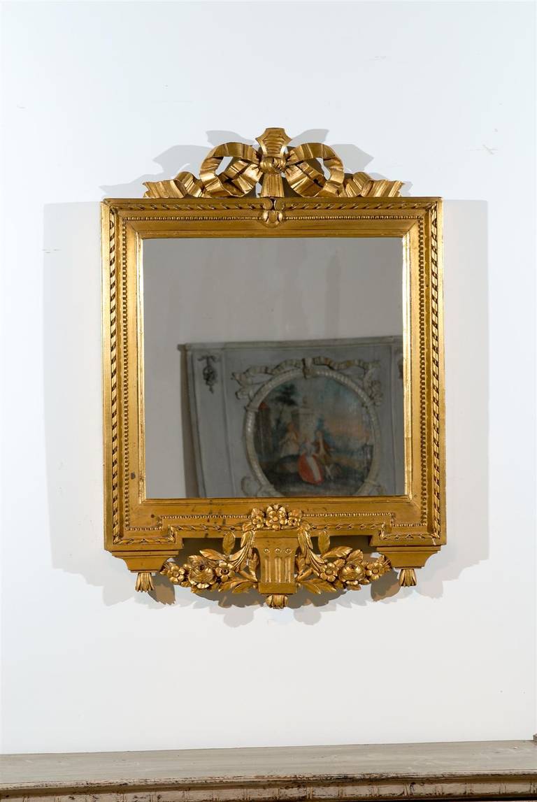 A Swedish Gustavian period giltwood mirror from the late 18th century with ribbon-carved crest and floral décor. This Swedish wall mirror features a rectangular giltwood frame, adorned with delicate beads and a twisted ribbon molding surrounding the