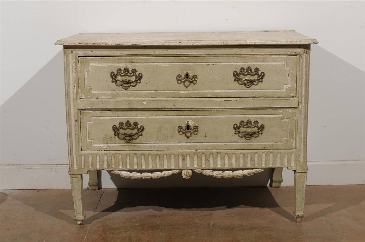 A French Louis XVI period two-drawer commode with marbleized top and carved swag from the late 18th century. This French commode features a faux-marble rectangular top with beveled edges sitting over two drawers. Each drawer is adorned with a