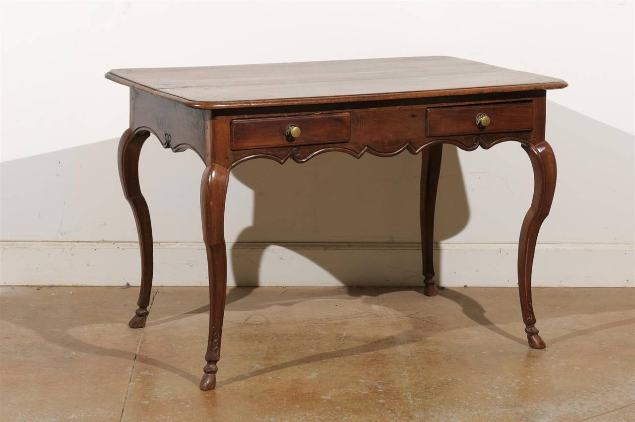 A French Louis XV period wooden writing table with two drawers, cabriole legs and scalloped apron from the mid-18th century. This French desk features a rectangular top with rounded edges, surmounting two short hand-cut dovetailed drawers. The apron