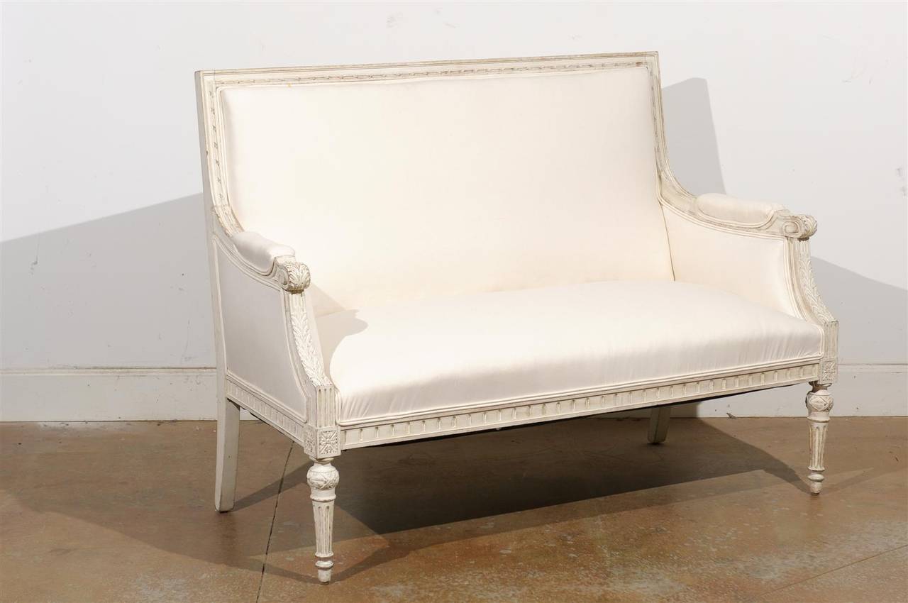 A Swedish neoclassical Revival carved and painted two-seat sofa from the late 19th century with new upholstery. This Swedish sofa features a slightly slanted rectangular back, framed by two partially upholstered scrolled arms, adorned with acanthus