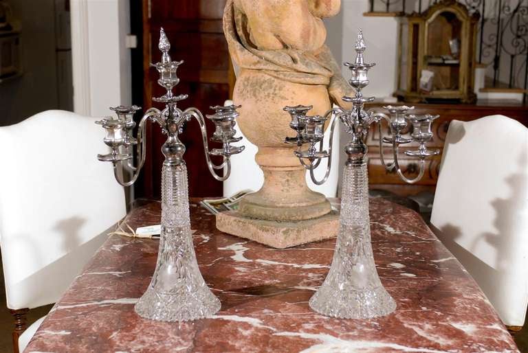 A pair of American silver and cut-glass four-arm candelabras by Derby Silver Company from the early 20th century. Each of this pair of candelabras features an exquisite cut-glass base, adorned with a profusion of delicate motifs. Typical of the