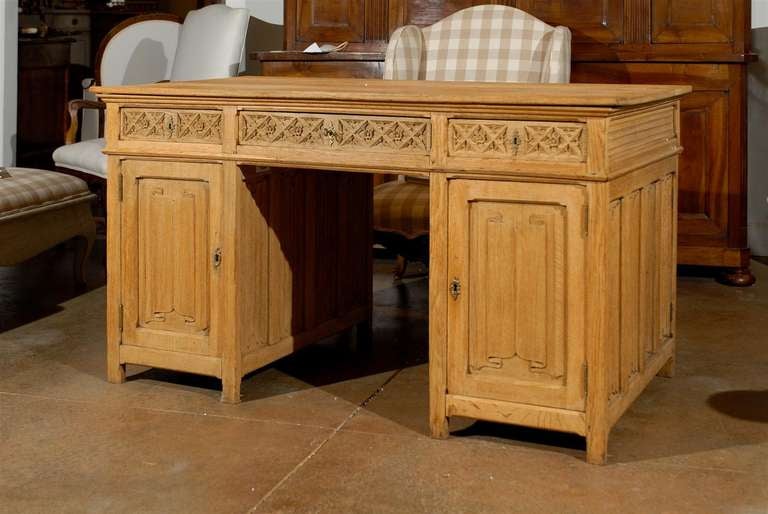 An English bleached oak Gothic Revival desk with linenfold motifs from the first half of the 19th century. This English desk features a rectangular top over three drawers and two side cabinets. The late Gothic influence, particularly praised during