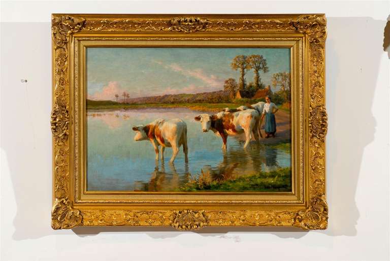 A French pastoral oil painting from the late 19th century by Félix Planquette (1873-1964), depicting a peasant with her cows at a river, set in a giltwood frame. This exquisite French painting features a pastoral scene, organized around three cows