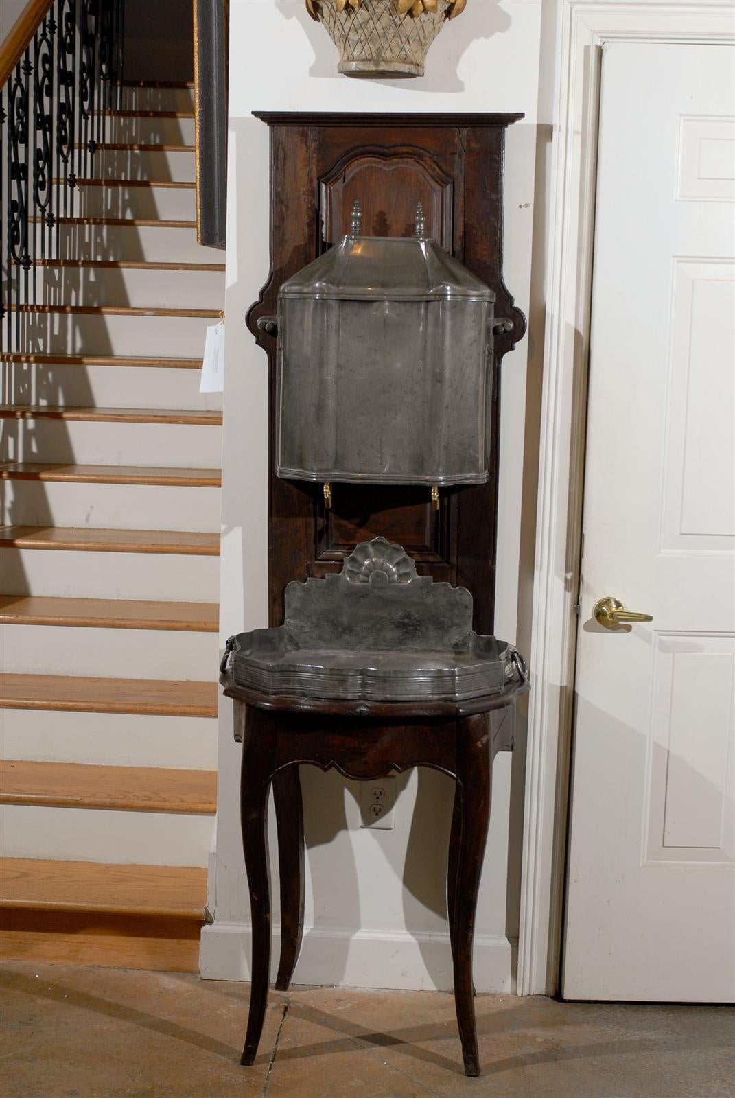 A French pewter two-part lavabo mounted on a walnut stand from the first half of the 19th century. Born at the point of transition between the Restauration period and the Louis-Philippe reign, this exquisite French 'fontaine' features a walnut body