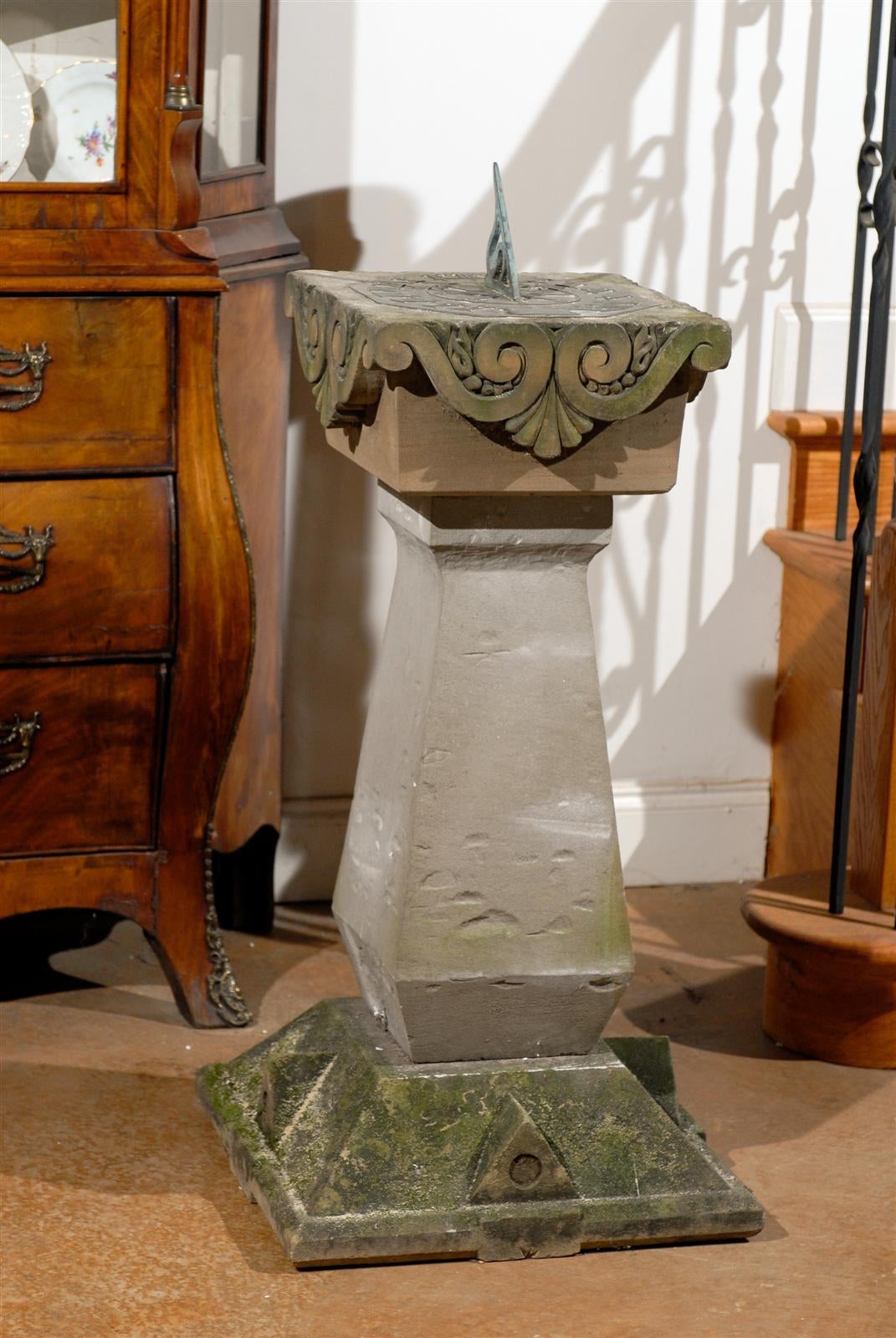 An English sundial from the late 19th century, with carved limestone and bronze top. This English sundial features an obelisk-shaped base, raised on a pyramidal plinth, with cut-off top. Each side is adorned with triangular motifs reminiscent of