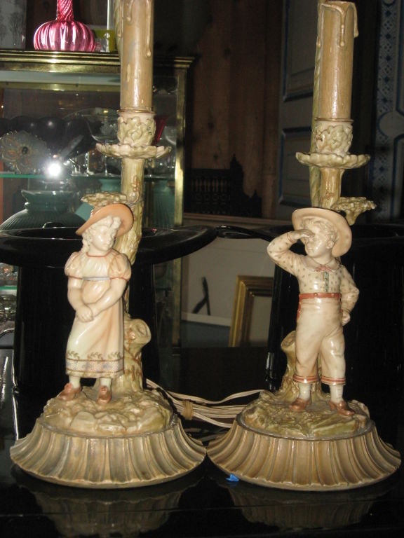 Pair of Royal Worcester porcelain candlesticks of a children made into lamps with harps and finials not shown.
