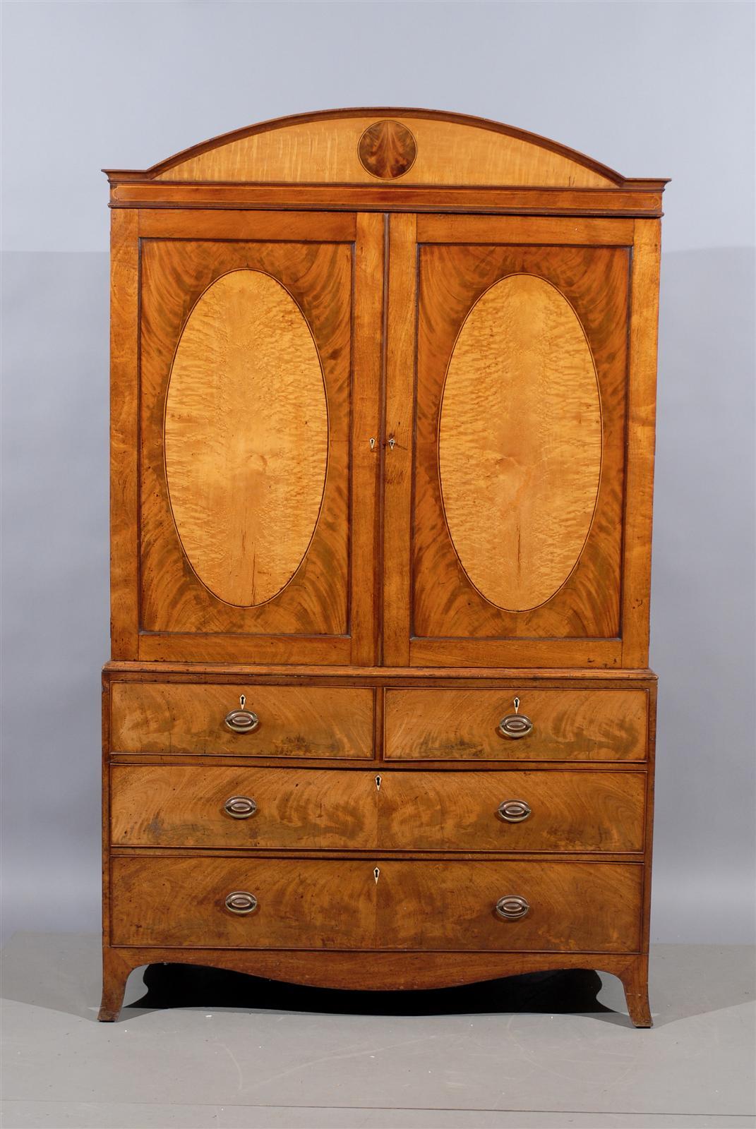 A George III English linen press in mahogany with satinwood arched cornice and oval veneered doors with interior shelf . The lower section with four sliding drawers, shaped apron and splayed feet. 

William Word Fine Antiques: Atlanta's source for