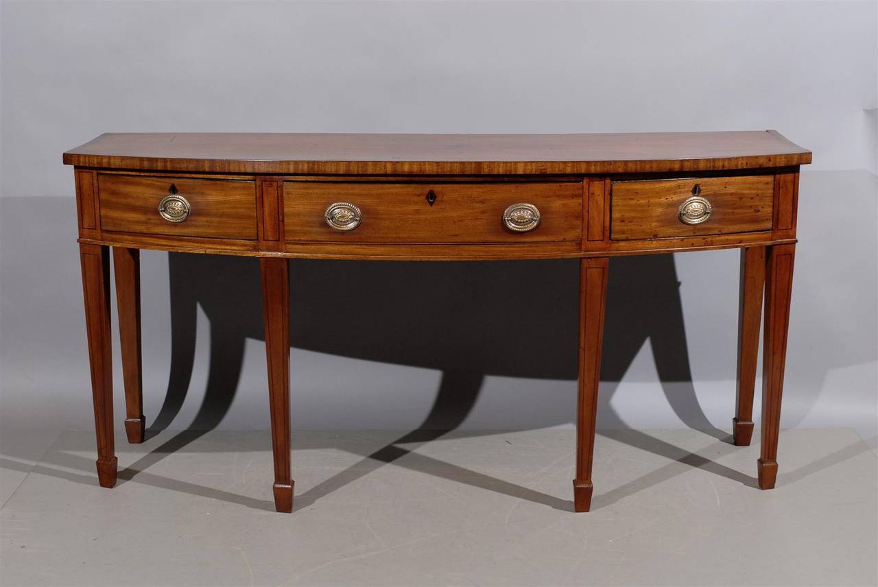 An English mahogany bow front server with string inlay, crossbanding and three drawers with brass pulls. 

William Word Fine Antiques: Atlanta's source for antique interiors since 1956.