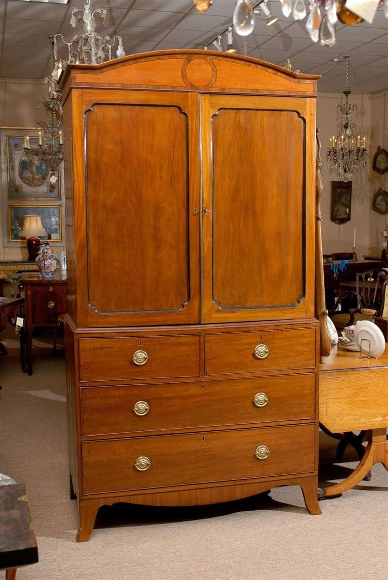 A Sheraton style mahogany linen press with arched inlaid cornice, cabinet doors with ebony detail, 4 sliding drawers with brass pulls and shaped apron with splayed feet below. 

William Word Antiques: Atlanta's source for antique interiors since