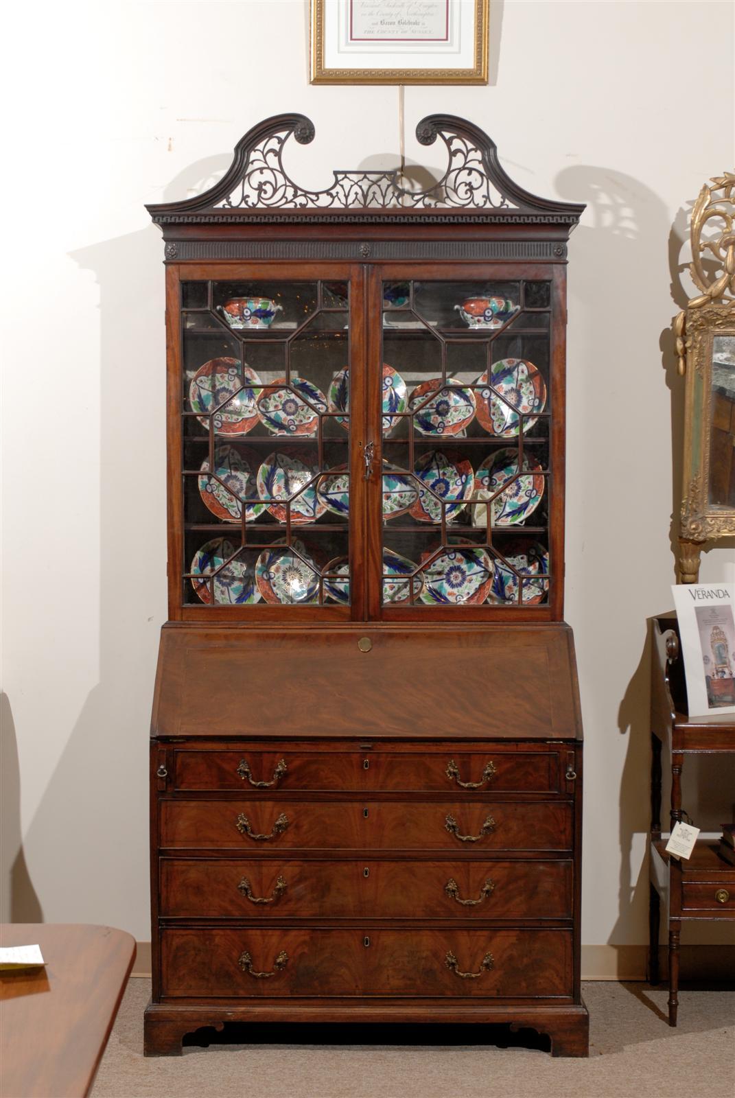 An 18th century George III mahogany bureau bookcase with fretwork swan neck pediment, glazed doors with geometric 15 pane sash work, slant front enclosing a fitted interior above five drawers and bracket feet. English in origin and dating from the